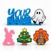 Blue personalized Namelet desk sign with ghost, Christmas tree, pink bunny, and turkey interchangeable Sidekicks displayed in front.