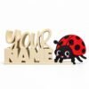 Cream-colored personalized stacked Namelet with script lettering, paired with a cheerful red and black ladybug Sidekick featuring pink cheeks and black spots, displayed on a clean white background.
